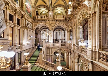 I visitatori scendono gradini di pietra tappezzati di verde sotto volte affrescate e statue nel foyer neo-renaissance della Wiener Staatsoper, Vienna. Foto Stock