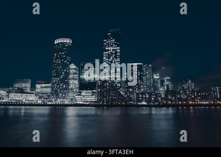 Skyline di Canary Wharf di notte riflessa nell'acqua liscia del Tamigi, esposizione lunga, Londra, Regno Unito Foto Stock