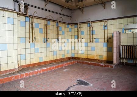 Una vista atmosferica di un'antica sala docce all'interno di un edificio industriale abbandonato nell'ex Germania Est. Pareti erose, accessori invecchiati e l'interno vuoto rivelano il trascorrere del tempo e il carattere dimenticato di un ex posto di lavoro industriale. L'im Foto Stock