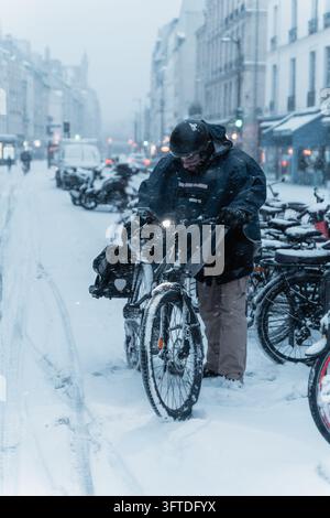 Parigi, Francia, 7 gen, 2026. Un uomo controlla la sua bicicletta tra biciclette coperte di neve in una forte nevicata. Foto Stock