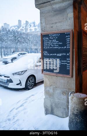 Parigi, Francia, 7 gen. 2026. Una tabella del menu di un ristorante sotto gli archi della innevata Place des Vosges. Foto Stock