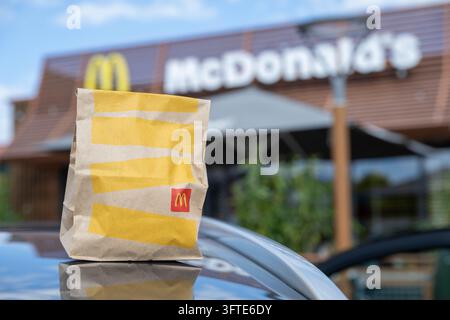 Un sacchetto di carta di McDonald's sul tetto di un'auto, il cartello del ristorante dietro. Immagine simbolica per il fast food, il takeaway e la tassa sugli imballaggi. Schifferstadt, Germania, 1 Foto Stock