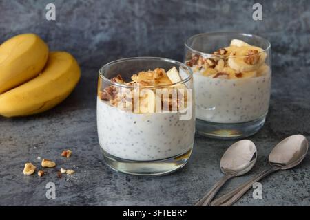 Budino ai semi di chia con banana e noci in bicchieri su sfondo scuro Foto Stock
