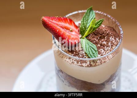 Dessert tiramisù in un bicchiere guarnito con una fetta di fragola fresca e foglie di menta Foto Stock