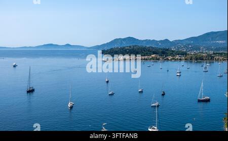Barche a vela e yacht ancorati nella calma baia blu di Garitsa sotto le colline verdi e la costa di Corfù, Grecia, vista dalla Vecchia Fortezza Foto Stock