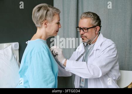 Medico di mezza età che esamina un paziente di mezza età con lo stetoscopio Foto Stock