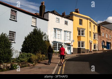 Una fila di case a schiera colorate a Ross-on-Wye costeggia una strada tranquilla su un pendio sotto un cielo azzurro. Le case presentano finestre a ghigliottina e a bovindo. Foto Stock