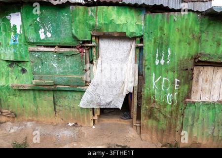 Muro in lamiera ondulata dipinto di verde patinato con una tenda di pizzo in una porta nell'area di Kibera, Contea di Nairobi, Nairobi, Kenya Foto Stock