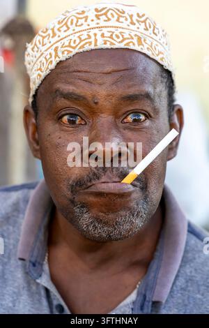 Ritratto ravvicinato di un uomo con un berretto kofia ricamato, una sigaretta in bocca e occhi grandi ed espressivi, Stone Town, Tanzania Foto Stock