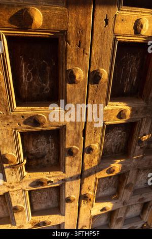 Primo piano di pannelli di porta in legno vecchio e consumato con grandi borchie di ferro e segni di gesso nella calda luce dorata del tramonto, Stone Town, Tanzania Foto Stock