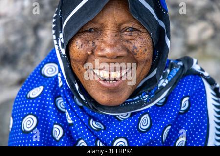 Ritratto ravvicinato di una donna anziana che ride con una pelle rugosa e lentigginosa e un dente mancante, in un kanga a pois blu, Matemwe, Tanzania Foto Stock