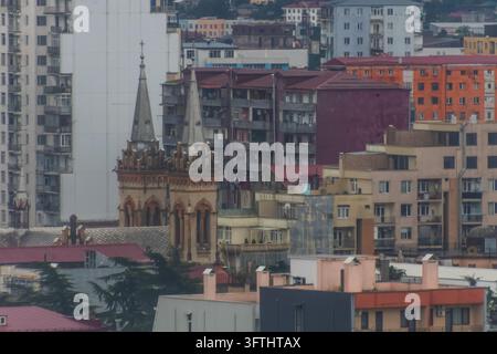 Scatto dettagliato delle elaborate guglie gemelle in pietra della Cattedrale della Sacra Madre Vergine della Natività circondata da case residenziali a Batumi, Georgia.... Foto Stock