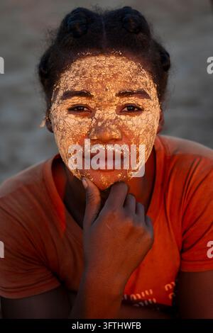 Una giovane donna con una maschera di bellezza in argilla screpolata appoggia il mento sulla mano al tramonto, Menabe, Tsiribihina, Madagascar Foto Stock