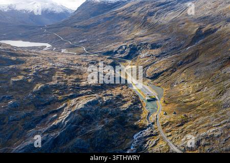 Vista aerea della strada di montagna Trollstigen, con area parcheggio e edifici per turisti, che si snoda attraverso il paesaggio aspro con vette innevate Foto Stock