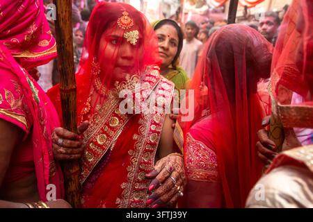 Donna in un sari velato rosso con gioielli tiene un lathi di bambù tra le donne al Lathmar Holi, Uttar Pradesh, Barsana, India Foto Stock