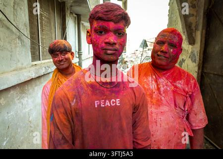 Tre uomini sorridenti con gulal rosa e arancione sul viso e sui vestiti posano insieme, Uttar Pradesh, Vrindavan, India Foto Stock
