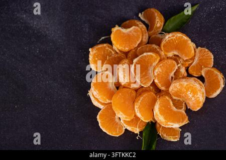 Vista dall'alto di segmenti di mandarini ammucchiati su uno sfondo rustico. Cibo scuro di mandarini Foto Stock