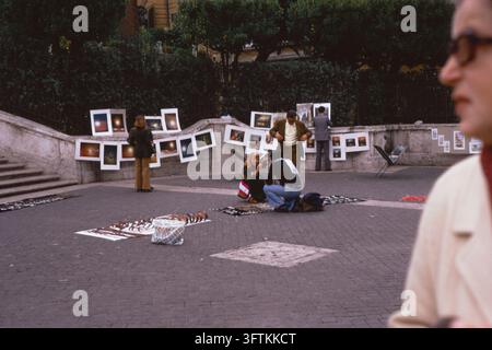 Artisti di strada che espongono dipinti sulla terrazza in cima alla Scalinata di Spagna, con una donna in primo piano, Roma, Italia, novembre 1973. Foto Stock