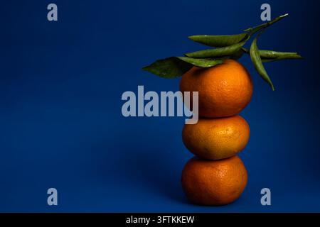 Mandarini freschi impilati su uno sfondo blu scuro. cibo scuro Foto Stock