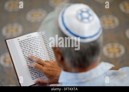 Un uomo anziano che indossa una kippah segue con il dito mentre legge un passaggio della Torah scritto in ebraico durante la sua sessione di lettura. Foto Stock