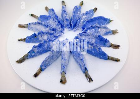 Ravioli asiatici blu ripieni di gamberetti sono disposti con cura in cerchio su un piatto bianco rotondo prima di essere cotti. Foto Stock