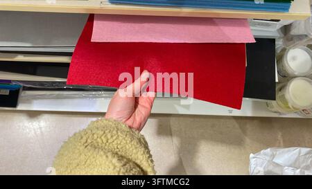 Primo piano della mano di un cliente che seleziona un foglio di tessuto di feltro rosso da un assortimento di materiali per il fai-da-te colorati in un negozio di articoli artistici Foto Stock