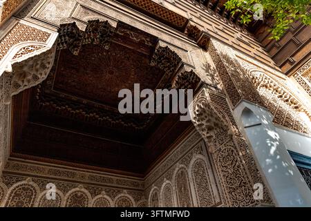 Una vista dettagliata a bassa angolazione che si concentra sulle spettacolari intagli geometrici in legno e sugli ornamenti in gesso arabeschi all'interno del Palazzo Bahia a Marrakesh.... Foto Stock