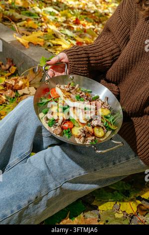 Donna che tiene una padella di pesce e verdure all'aperto in autunno Foto Stock