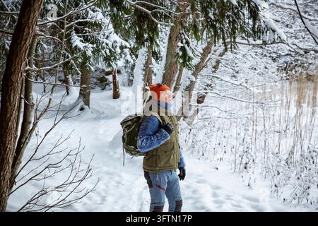 Un escursionista maschio cammina lungo un sentiero boschivo innevato accanto a una parete di granito, un'avventura invernale attiva nella natura finlandese incontaminata Foto Stock
