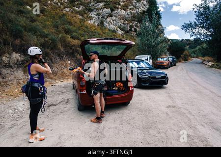 Coppia avventurosa che organizza l'attrezzatura dal bagagliaio dell'auto, preparandosi per l'arrampicata su roccia in un paesaggio montano impervio Foto Stock