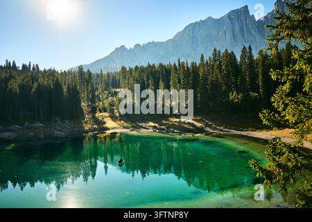 Barca a remi su un lago alpino smeraldo all'alba con riva boschiva e cresta montuosa frastagliata nella morbida luce del mattino, scena in stile Dolomiti per la natura Foto Stock