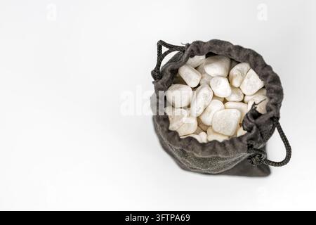 Borsa grigia con cordoncino aperta per mostrare ciottoli bianchi lisci su sfondo bianco, simboleggiando mistero, tesoro nascosto e valore incerto all'interno. Foto Stock