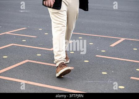 Un individuo attraversa un labirinto dipinto su un'area pavimentata, simboleggiando movimento giocoso, infrastrutture educative, svago all'aperto e impegno Foto Stock