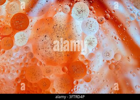 Affascinante fotografia macro di gocce d'olio che galleggiano sull'acqua, formando bolle sferiche colorate in tonalità arancioni vivaci, ambra, bianco e blu morbido Foto Stock
