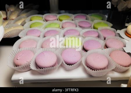 Close-up di macarons pastello disposti in bicchieri di carta su un vassoio da esposizione, che mostra file di biscotti sandwich rosa e verdi con gusci lisci e bombati, croccante Ed Foto Stock