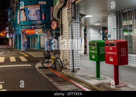 Città di Taipei, Taiwan - 06 giugno 2015: Vista di un angolo di strada di notte con una bicicletta gialla parcheggiata vicino a cassette postali rosse e verdi accanto a un edificio con piastrelle Foto Stock