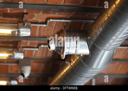 Condotti d'aria metallici corrono sotto un soffitto di mattoni, con luci visibili all'interno. Foto Stock