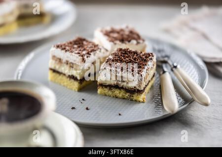 Deliziose torte a strati con panna, banane e panna montata soffice servite su un piatto elegante. La parte superiore dei dessert è cosparsa di gra finemente macinata Foto Stock
