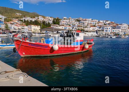 Andros, Grecia - 21 maggio 2026: Barca da pesca rossa ormeggiata nel porto del villaggio di Batsi Foto Stock