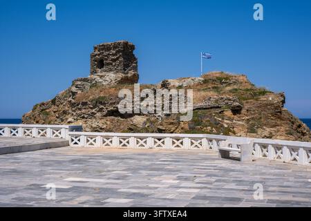 Andros, Grecia – 21 maggio 2026: Rovine del castello di Andros arroccate su uno sperone roccioso sopra il Mar Egeo con bandiera greca Foto Stock