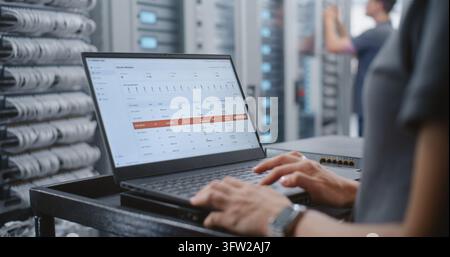 Specialista femminile del data center monitora il dashboard del server mentre appare un avviso critico di surriscaldamento, rivedendo la temperatura, il carico della CPU, la memoria e il traffico di rete mentre avvia le procedure di risposta agli incidenti. Foto Stock