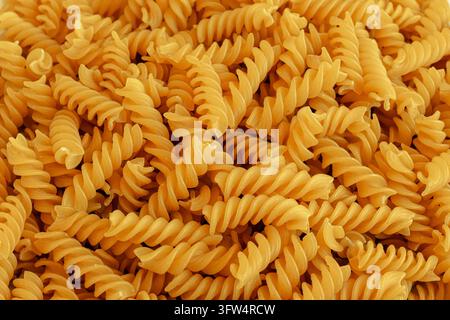 Primo piano di un mucchio di pasta spirale cruda che riempie il fotogramma con un colore giallo caldo e creste attorcigliate testurizzate, vista dall'alto per: Foto Stock