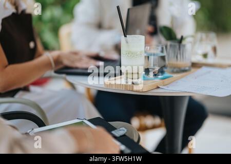 Colleghi che hanno una riunione di lavoro in un caffè con laptop e bevande sul tavolo. Una sessione di lavoro informale mostra persone che collaborano davanti a un drink, Foto Stock