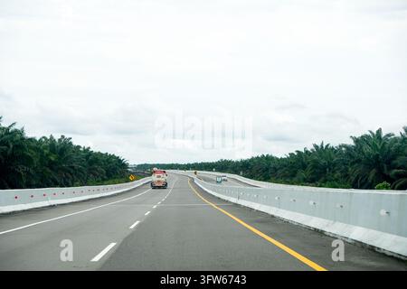 Riau, Indonesia - 27 dicembre 2025: Strada a pedaggio moderna asfaltata e camion che attraversa una piantagione di olio di palma sull'autostrada Pekanbaru-Dumai Foto Stock