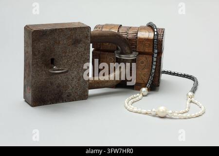 Grande serratura a padlock bloccata con una chiave e un baule del tesoro in miniatura intagliato. Gioielli di imitazione. Sfondo neutro. Foto Stock