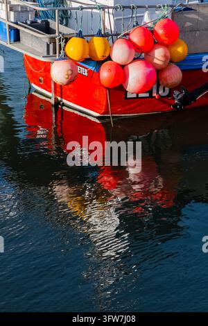 Poppa di un peschereccio rosso acceso con boe colorate che si riflettono nelle increspature dell'acqua calma del porto di West Bay Harbour, Dorset, Inghilterra, Regno Unito Foto Stock