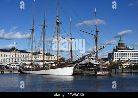 Helsinki, Finlandia – 07 ottobre 2026: Vecchie navi a vela ormeggiate lungo il lungomare del porto di Helsinki, con la cattedrale di Uspenski in mattoni rossi che si erge Foto Stock