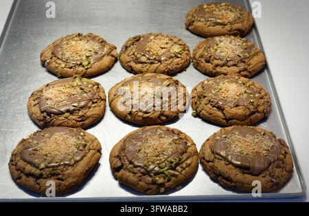 Biscotti gourmet appena sfornati ricoperti di glassa al cioccolato, pistacchi e kadayif, serviti su un vassoio di metallo in una panetteria di Colonia Foto Stock