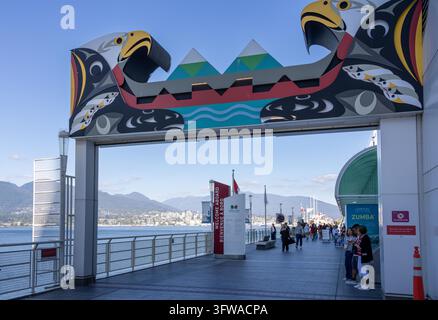 Vancouver, Canada – 8 settembre 2026: Ripresa orizzontale a livello degli occhi dell’arco stilizzato indigeno che incornicia i turisti lungo la passeggiata del lungomare con Foto Stock