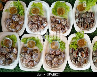 Le cozze Hoy Klang e le conchiglie di mela nera Hoy Khong vengono servite con salsa da intingere e lattuga in una bancarella di mercato thailandese. Foto Stock